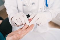 De dessus de la culture méconnaissable médecin dans des gants stériles en prenant un test sanguin du patient avec lancette à l'hôpital — Photo de stock