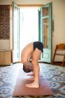 Vista lateral de macho anónimo flexible con torso desnudo de pie en Prasarita Padottanasana mientras practica yoga y estira el cuerpo en casa - foto de stock