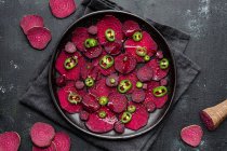 Top view composition of tasty beetroot slices arranged on baking pan with green jalapeno peppers and placed on black towel on kitchen table — Stock Photo
