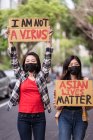 Этнические женщины в масках держат плакаты с протестами против расизма на городской улице и отворачиваются — стоковое фото
