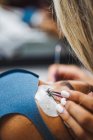 Ernte unkenntlich Kosmetiker mit Pinzette Anwendung gefälschte Wimpern für die Verlängerung auf das Auge des ethnischen Kunden mit Gesichtsschutzmaske im Salon während der Coronavirus-Pandemie — Stockfoto