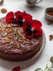 Зверху солодкий шоколадний торт, прикрашений червоними квітами та волоськими горіхами, що подаються на столі — стокове фото