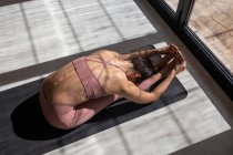 D'en haut femelle méconnaissable dans les vêtements de sport effectuer Pascimottanasana pose tout en pratiquant le yoga sur tapis dans la maison — Photo de stock