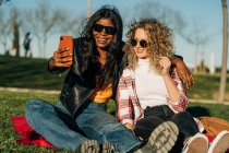 Allegro multirazziale migliori amici femminili abbracciando in giardino primaverile e prendendo auto colpo su smartphone nella giornata di sole — Foto stock
