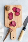 Zusammensetzung von reifen rohen Rote-Bete-Scheiben auf einem Holzschneidebrett auf dem Küchentisch in der Nähe eines scharfen Messers — Stockfoto