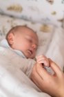 Crop anonymous parent with cute sleeping newborn child holding hands at home on blurred background — Stock Photo