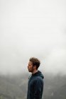 Vista laterale pensoso escursionista maschio in piedi sulla cima della montagna in altopiani a Siviglia sul tempo nebbioso nuvoloso — Foto stock