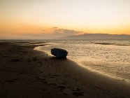 Спокойный морской пейзаж со старой рыбацкой лодкой, пришвартованой на песчаном пляже возле спокойного моря на закате — стоковое фото