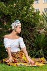 Allegro giovane femmina etnica in gonna africana ornamentale contro le piante di palma sul prato — Foto stock