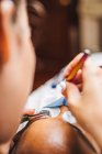 Ernte unkenntlich Kosmetiker mit Pinzette Anwendung gefälschte Wimpern für die Verlängerung auf das Auge des ethnischen Kunden mit Gesichtsschutzmaske im Salon während der Coronavirus-Pandemie — Stockfoto