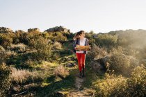 Full body of focused young female explorer in casual clothes reading map while walking on mountain slope on sunny day — Stock Photo