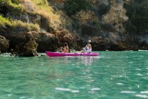 Viajeros de vista lateral con remos flotando en agua de mar turquesa cerca de la costa rocosa en un día soleado en Málaga España - foto de stock