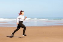 Vue latérale de joggeuses actives courant sur le rivage de l'océan pendant l'entraînement en été — Photo de stock