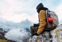 Боковой вид туриста с рюкзаком и в теплой одежде, стоящего на скалистом хребте долины в вершинах Европы и смотрящего в сторону — стоковое фото