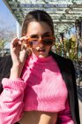Приваблива молода жінка в джинсах рожевий светр і чорне пальто стоїть з руками в кишенях біля столу в ресторані і дивиться на камеру — стокове фото