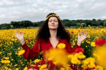 Concentrated female in flower wreath practicing yoga with closed eyes among blossoming daisies and Papaver on meadow in countryside — Stock Photo