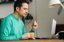 Seitenansicht männlicher Fernarbeiter mit Becher Heißgetränk gegen Netbook im Haus — Stockfoto