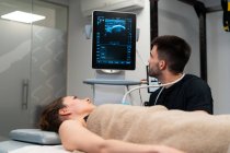 Médico varón revisando el pecho de la mujer en el monitor de la máquina de ultrasonido en el hospital - foto de stock