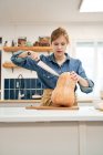 Joven hembra con cuchillo afilado cortando calabaza cruda en la tabla de cortar mientras cocina en casa - foto de stock