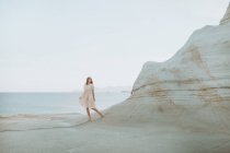 Donna in sundress bianco passeggiando lungo stretto passaggio formato da rocce curvy luce sul tempo soleggiato in Sarakiniko Grecia — Foto stock