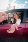Crop unrecognizable person passing vehicle key to content young female driver from modern automobile in city — Stock Photo