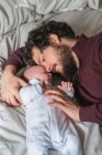 Высокий угол бородатого папы, обнимающего милого маленького ребенка, лежащего на измятой кровати и смотрящего друг на друга — стоковое фото