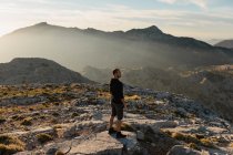 Side view of thoughtful male hiker in casual wear resting on rocky mountain summit and admiring scenic views over rough highlands in Seville Spain — Stock Photo