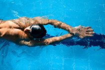 Vista dall'alto dell'atleta maschio in cuffia da bagno con braccia sollevate che nuota sulla schiena in piscina durante l'allenamento — Foto stock