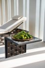 Plate with fresh green apples limes and bunch og grapes placed on small coffee table near comfortable lounger in sunlight — Foto stock