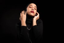 Приваблива молода ісламська жінка в чорному одязі і хіджаб торкається обличчя м'яко з закритими очима — стокове фото