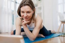Deliziosa femmina magra sdraiata su tappetino e tablet di navigazione durante la scelta della lezione online per praticare yoga — Foto stock