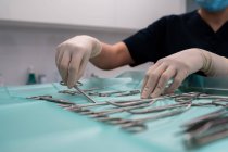 Crop unrecognizable veterinarian in latex gloves preparing assorted surgical tools on table against paws of canine patient in clinic — Stock Photo
