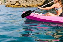 Seitenansicht eines unkenntlichen Reisenden mit Paddeln, die an einem sonnigen Tag in Malaga auf türkisfarbenem Meerwasser in der Nähe der felsigen Küste schwimmen — Stockfoto