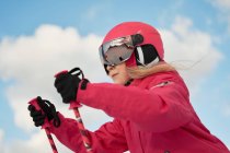 Side view cute girl in pink warm activewear goggles and helmet skiing along snowy slope on clear winter day — стоковое фото