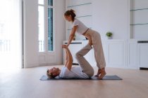 Side view of boyfriend lifting girlfriend while doing acro yoga together at home and holding hands — Foto stock