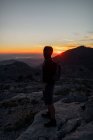 Escursionista maschio senza volto a tutta lunghezza con zaino ammirando panoramico terreno montagnoso e in piedi sulla vetta rocciosa ruvida al tramonto a Siviglia Spagna — Foto stock