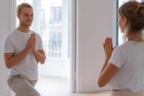 Side view of content couple in activewear standing on mats in Anjaneyasana with Namaste gesture while doing yoga in morning and looking at each other - foto de stock