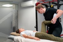 Erwachsener männlicher Physiotherapeut berührt Bein einer Frau mit geschlossenen Augen bei Untersuchung im Krankenhausbett — Stockfoto