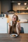 Cheerful young female with tasty oatmeal biscuit with chocolate chips for breakfast on table in kitchen — Stock Photo