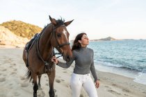Young female walking with chestnut stallion looking away against wavy ocean — Stock Photo