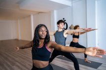 Donna afroamericana in compagnia di diverse persone che praticano yoga in Warrior due posa in studio — Foto stock