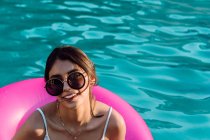 Junge fröhliche Reisende in Badebekleidung und Sonnenbrille liegen in aufblasbarem Ring im Schwimmbad — Stockfoto