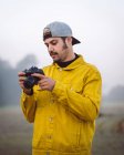 Young male photographer in yellow denim jacket taking photo on photo camera while standing on foggy blurred nature background — Stock Photo