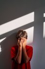 Upset unrecognizable boy covering face with hands and crying while standing near wall at home — Stock Photo