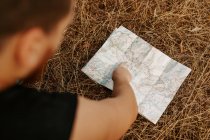 From above cropped unrecognizable male traveler pointing while looking into a map on the forest — Stock Photo