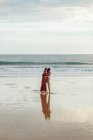 Liebender Mann umarmt Frau von hinten, während er den Sommertag zusammen am Strand verbringt — Stockfoto