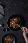 Vista dall'alto del raccolto persona irriconoscibile che prende cibo con bacchette da piatto con piatto coreano Japchae cucinato da tagliatelle e verdure — Foto stock
