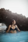 Vue latérale du jeune hipster tatoué en maillot de bain posant en eau bleue entre les rochers — Photo de stock