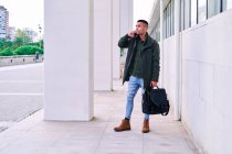 Full body Hispanic man in casual clothes looking away and speaking on mobile phone while standing on pavement before work — Stock Photo