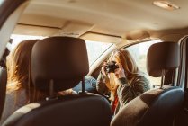 Frau mit Oldtimer-Kamera fotografiert Freundin beim Autofahren bei sonnigem Tag — Stockfoto